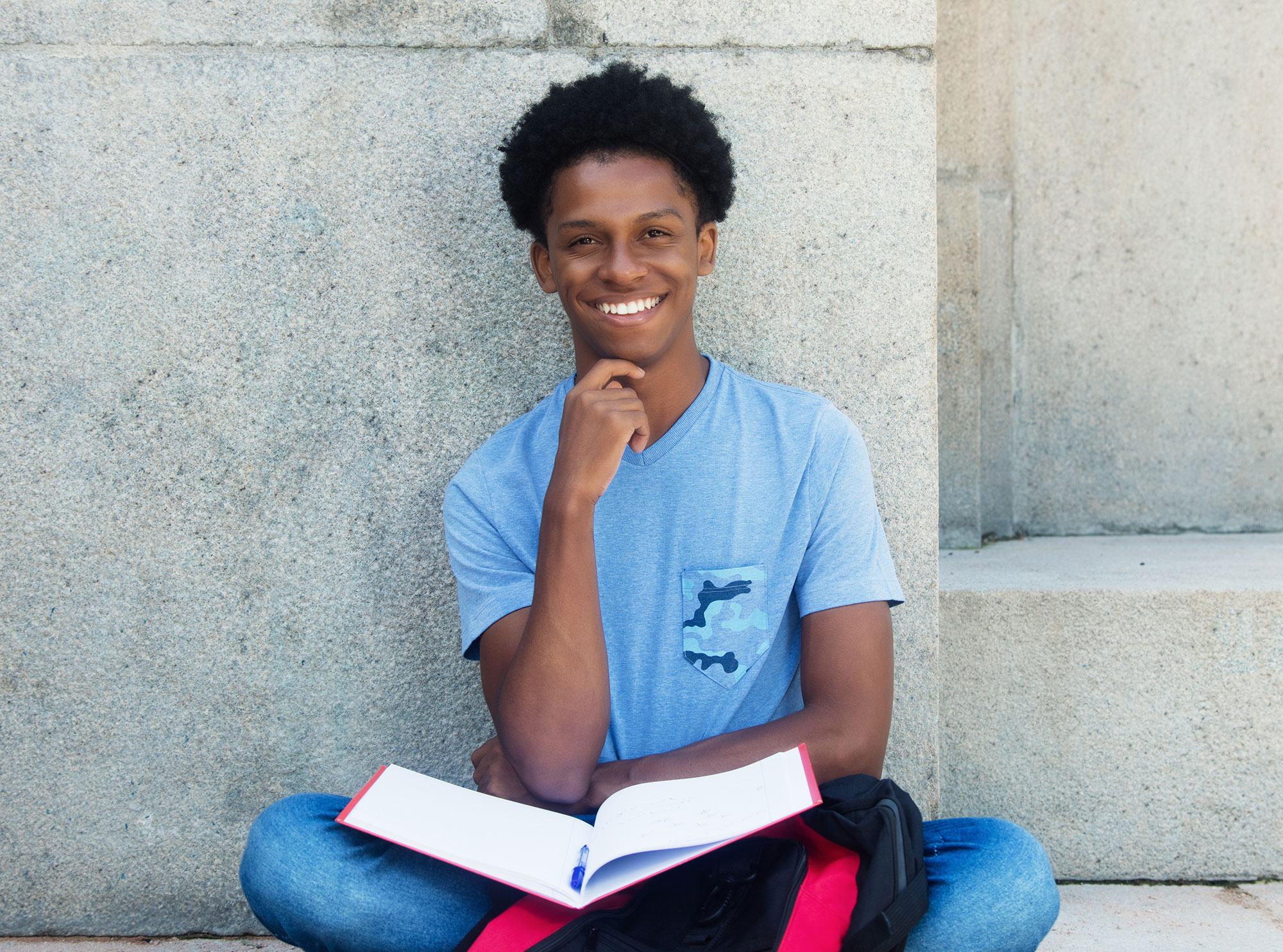 Teenage boy does his homework outside a building.